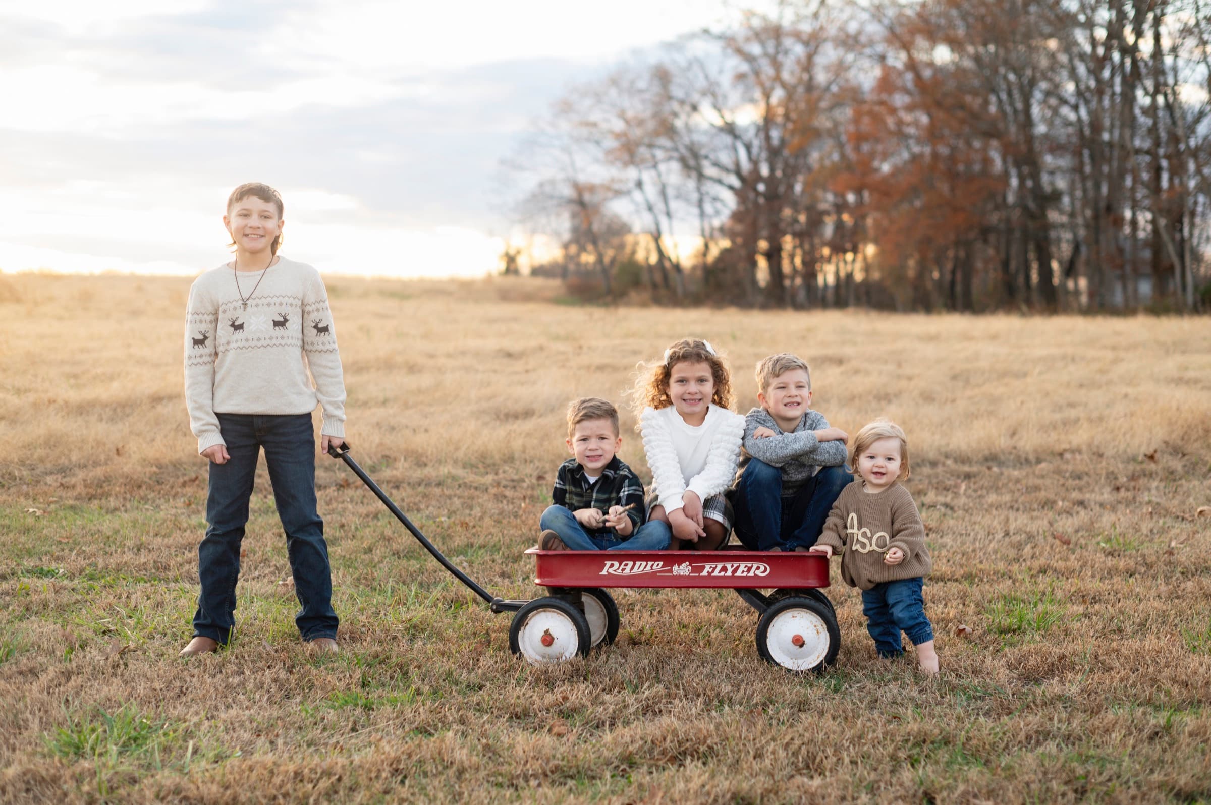 Children playing with a red wagon in a field