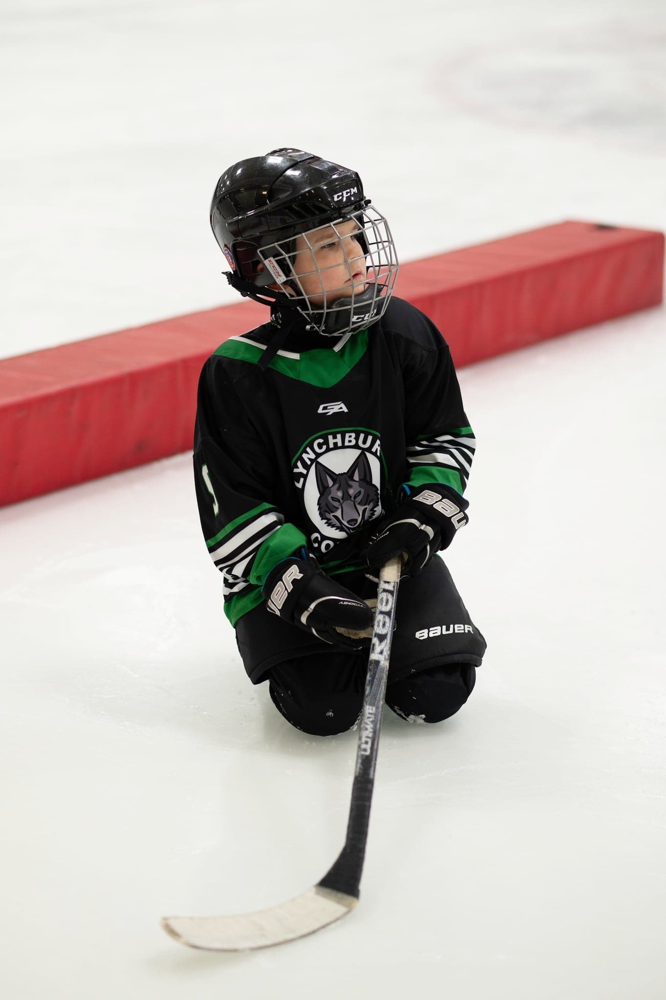 Coyotes player kneeling on the ice beside the boards, helmet on