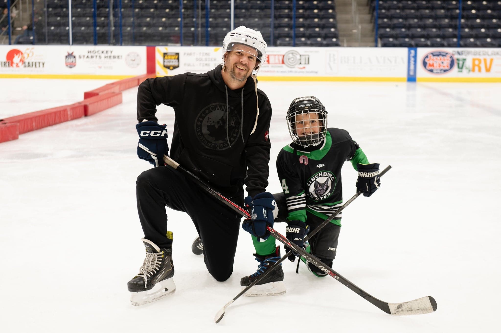Coach kneeling beside a young Coyotes player, both smiling on the ice